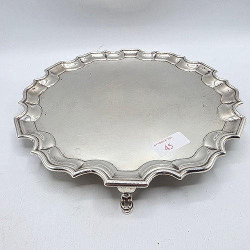 45 - A sterling silver card tray or salver with pie crust rim raised on three hoof feet. 26cm (d). By Jos... 