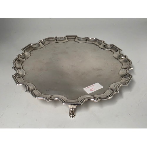 45 - A sterling silver card tray or salver with pie crust rim raised on three hoof feet. 26cm (d). By Jos... 