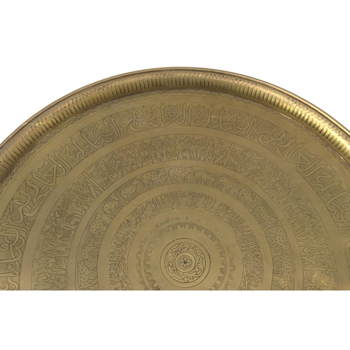 2058 - Middle Eastern brass tray topped circular occasional table decorated with figures and script, the tr... 