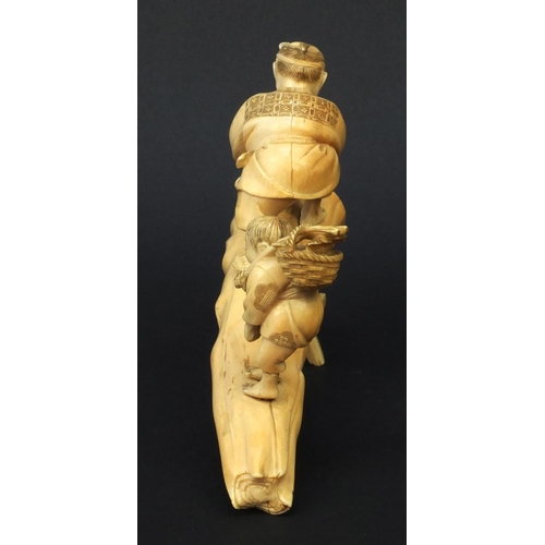 599 - Oriental Japanese carved ivory okimono of an elder and child standing on a tree trunk, the elder cut... 