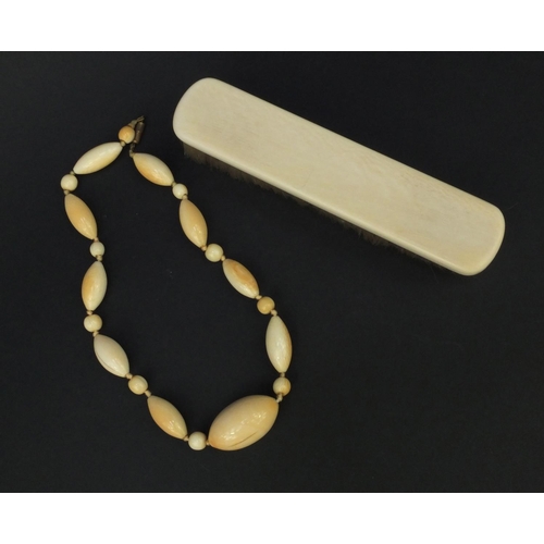 628 - Ivory beaded necklace and an ivory backed clothes brush, the largest bead 4cm diameter