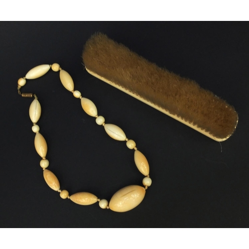 628 - Ivory beaded necklace and an ivory backed clothes brush, the largest bead 4cm diameter