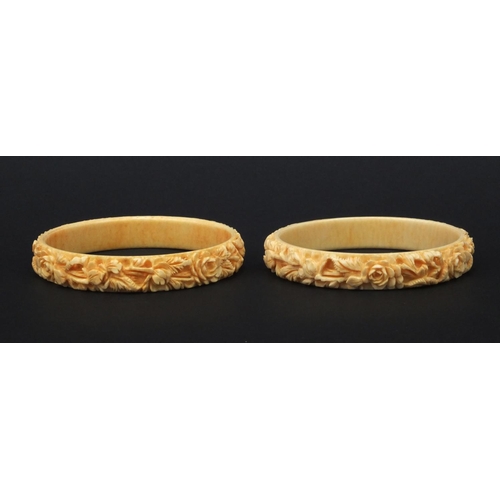 629 - Two oriental Chinese ivory bangles both carved with flowers, each 7.5cm diameter