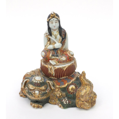 594 - Oriental Japanese satsuma pottery figure of a girl seated on a Buddhistic lion, 21cm high