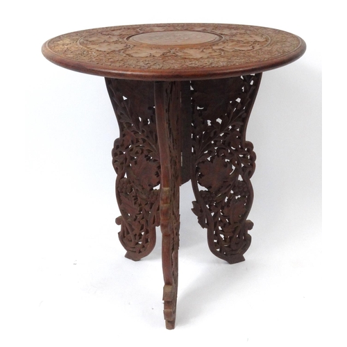 105 - Profusely carved Middle Eastern folding occasional table with brass inlay, 64cm high x 55cm diameter