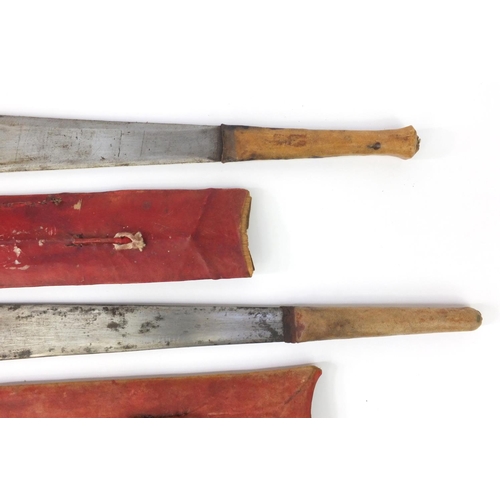 601 - Two Kenyan panga knifes with red sheaths, the longest 56cm long