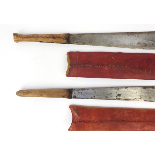 601 - Two Kenyan panga knifes with red sheaths, the longest 56cm long