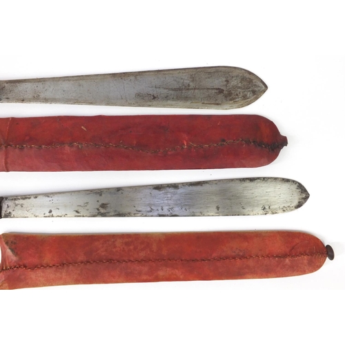 601 - Two Kenyan panga knifes with red sheaths, the longest 56cm long