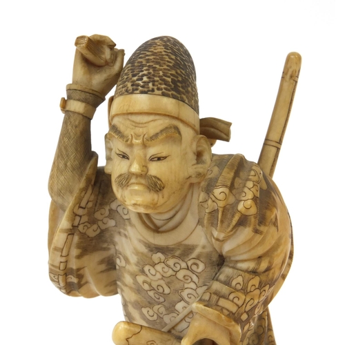 503 - Japanese finely carved ivory okimono of a samari warrior holding a katana and stick, signature to th... 