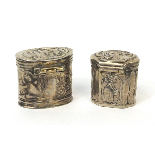 774 - Two unmarked silver trinkets with hinged lids, embossed with figures and putti, the larger 3.5cm hig... 