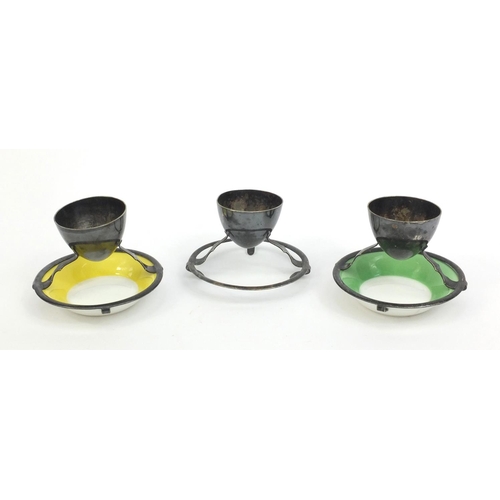 2149 - Three Hukin & Heath egg holders, two with Royal Doulton saucers, each 7cm high