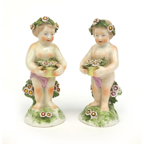 542 - Pair of porcelain cherub figures wearing floral garlands and holding baskets of flowers, gold anchor... 