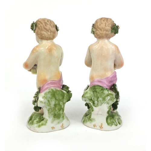 542 - Pair of porcelain cherub figures wearing floral garlands and holding baskets of flowers, gold anchor... 