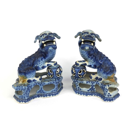 562 - Pair of delft blue and white pottery foo dogs, both raised on pierced floral bases, each 24cm high