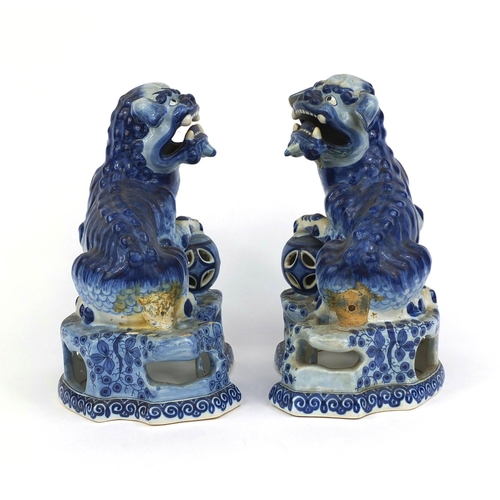 562 - Pair of delft blue and white pottery foo dogs, both raised on pierced floral bases, each 24cm high