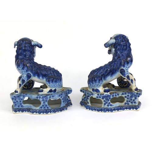 562 - Pair of delft blue and white pottery foo dogs, both raised on pierced floral bases, each 24cm high