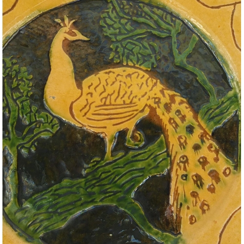 565 - Large pottery charger hand painted with a stylised peacock on a branch within a floral boarder, 37.5... 