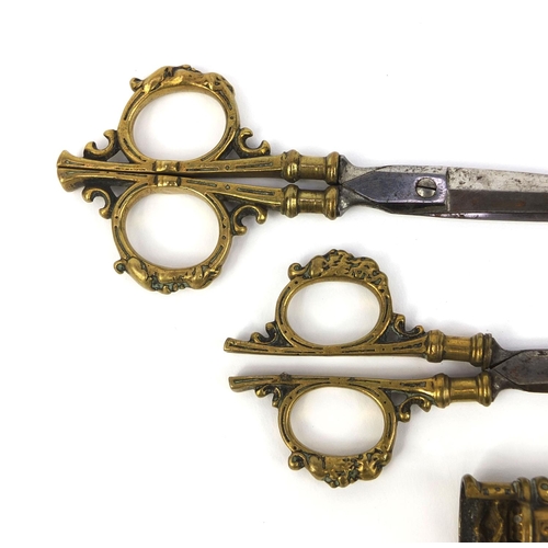 105 - Two pairs of 19th Century seamstress scissors housed in an ornate brass sheath, 16cm in length