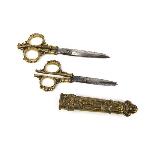 105 - Two pairs of 19th Century seamstress scissors housed in an ornate brass sheath, 16cm in length