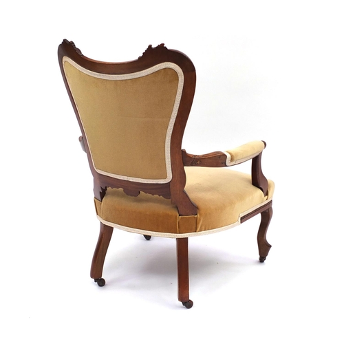 2053 - Carved walnut elbow chair with gold upholstery raised on cabriole legs and china castors, 88cm high