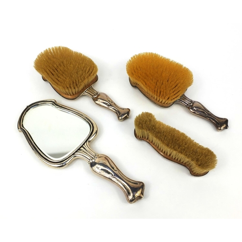 879 - Art Nouveau silver four piece dressing table set, comprising hand mirror and three brushes, each emb... 