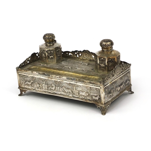 596 - Indian silver coloured metal desk stand with two inkwells and pierced gallery, profusely embossed wi... 