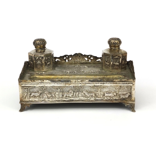 596 - Indian silver coloured metal desk stand with two inkwells and pierced gallery, profusely embossed wi... 