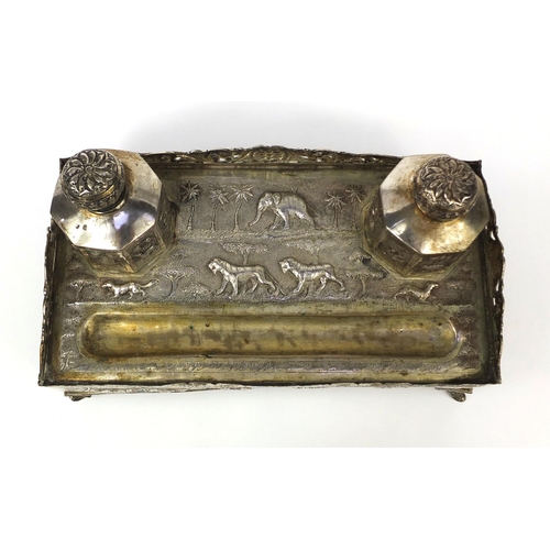 596 - Indian silver coloured metal desk stand with two inkwells and pierced gallery, profusely embossed wi... 