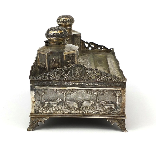 596 - Indian silver coloured metal desk stand with two inkwells and pierced gallery, profusely embossed wi... 