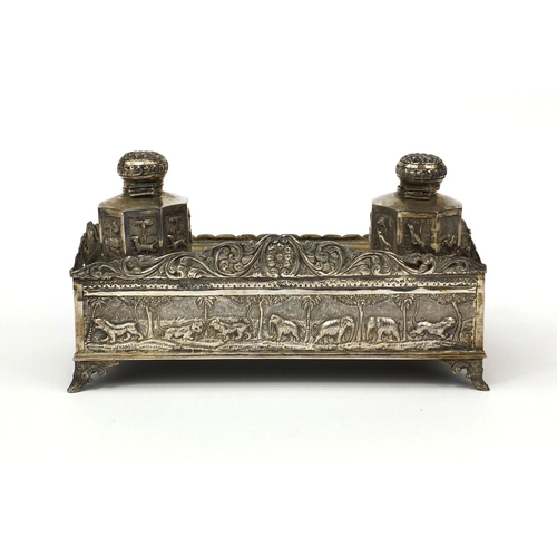 596 - Indian silver coloured metal desk stand with two inkwells and pierced gallery, profusely embossed wi... 