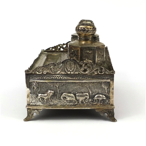 596 - Indian silver coloured metal desk stand with two inkwells and pierced gallery, profusely embossed wi... 