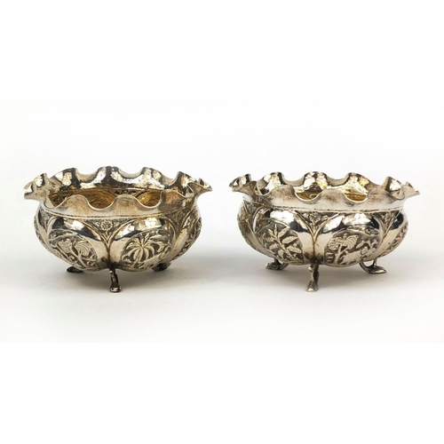 600 - Pair of Indian unmarked silver three footed bowls, each embossed with panels of animals and palm tre... 