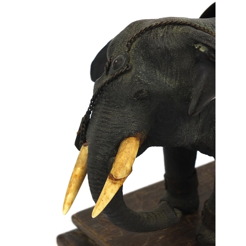 555 - Japanese bronze elephant with ivory tusks and Egyptian design seat, raised on a hardwood base, the e... 