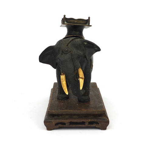 555 - Japanese bronze elephant with ivory tusks and Egyptian design seat, raised on a hardwood base, the e... 