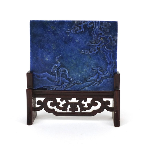 525 - Chinese Lapis Lazuli panel raised on a pierced hardwood stand, the panel carved with two cranes besi... 