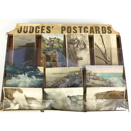 212 - Judges postcard wall display rack containing various local interest postcards including rough sea an... 