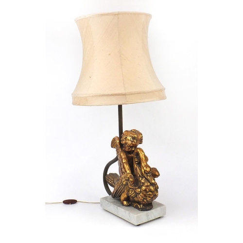 2243 - Ornate gilt lamp modelled as a putti riding a swan, with faux marble base, and silk lined shade, 76c... 