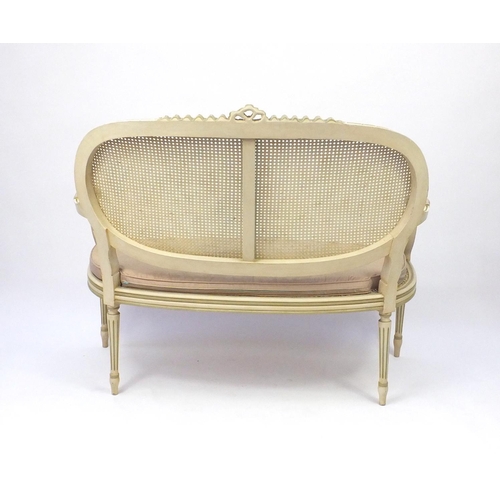 2011 - Cream and green painted two seater salon settee with cane panel back and seat, 103cm high x 120cm wi... 
