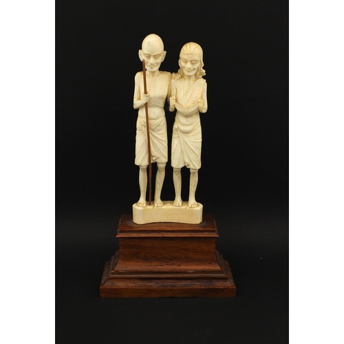 613 - Middle Eastern carved ivory group of two elders, one holding a stick, raised on a hard wood base, ov... 