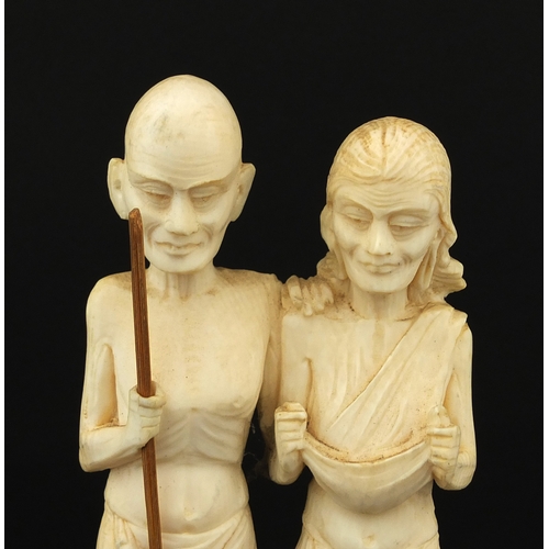 613 - Middle Eastern carved ivory group of two elders, one holding a stick, raised on a hard wood base, ov... 