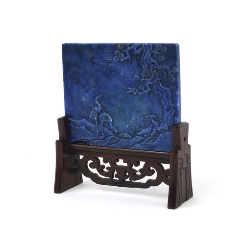 525 - Chinese Lapis Lazuli panel raised on a pierced hardwood stand, the panel carved with two cranes besi... 