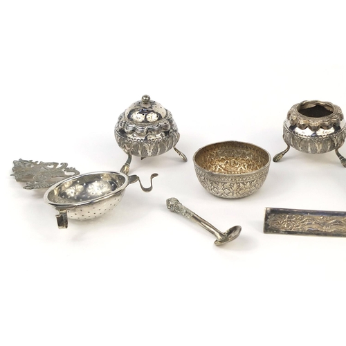 614 - Predominately Burmese silver coloured metal items including three piece cruet, strainer, triangular ... 