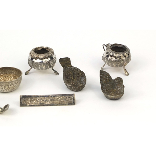 614 - Predominately Burmese silver coloured metal items including three piece cruet, strainer, triangular ... 