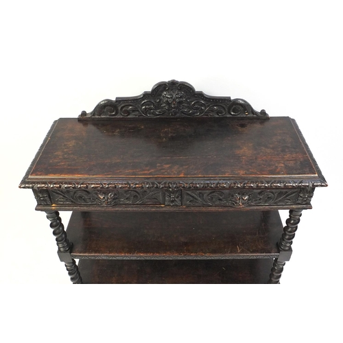 113 - Carved oak three tier buffet carved with lions heads and floral motifs, fitted with two frieze drawe... 