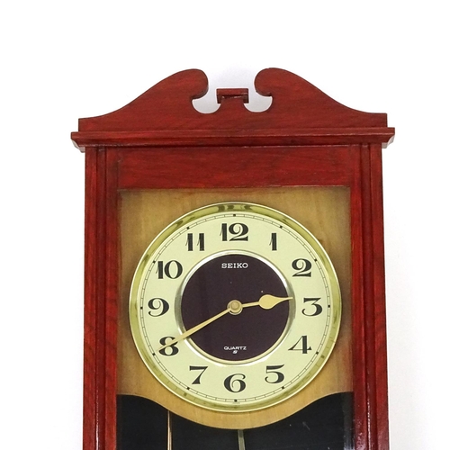 699 - Seiko mahogany wall hanging clock with visible pendulum, 53cm long