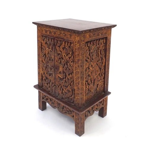 2043 - Indonesian hardwood side cabinet fitted with a pair of doors, carved with foliage, 56.5cm high x 39c... 