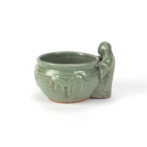 521 - Oriental celadon glazed pot with a figure beside, 12cm high x 16cm wide