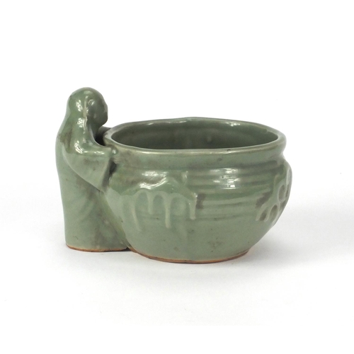 521 - Oriental celadon glazed pot with a figure beside, 12cm high x 16cm wide