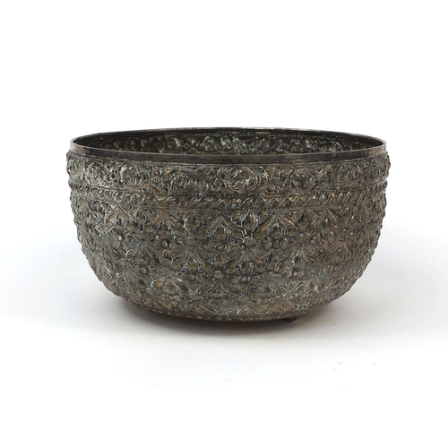 610 - Burmese silver three footed bowl profusely embossed with folaige, script to the base, 23cm in diamet... 