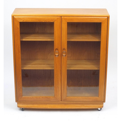 2019 - Ercol light elm book case fitted with a pair of glazed doors enclosing two adjustable shelves, label... 